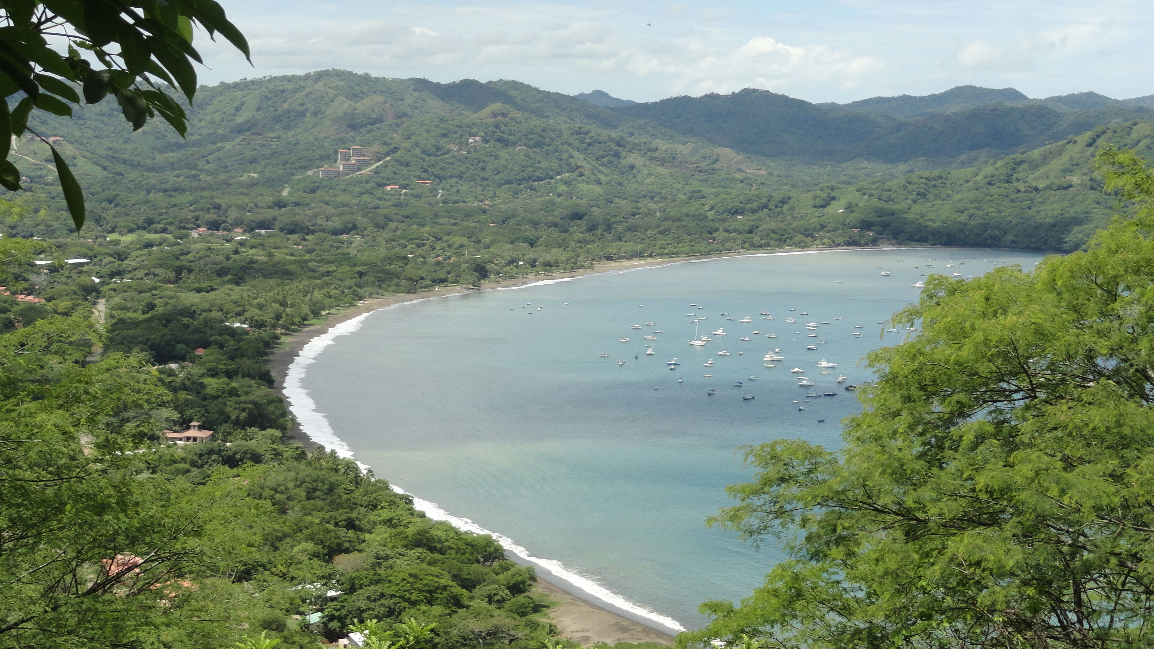 Un paisaje costero con playa, embarcaciones y colinas circundantes.