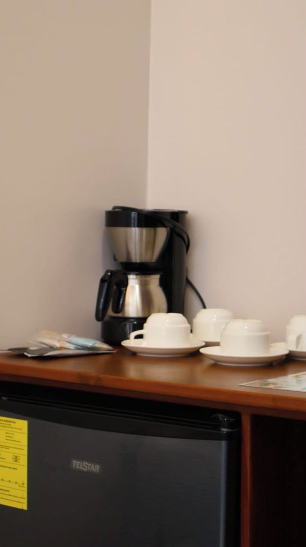 A coffee maker on a table with cups and saucers.