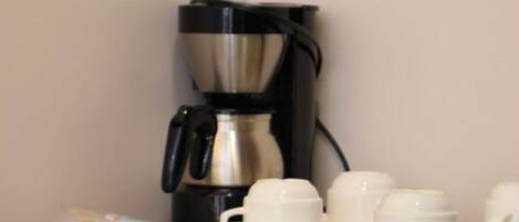 A coffee maker on a table with cups and saucers.