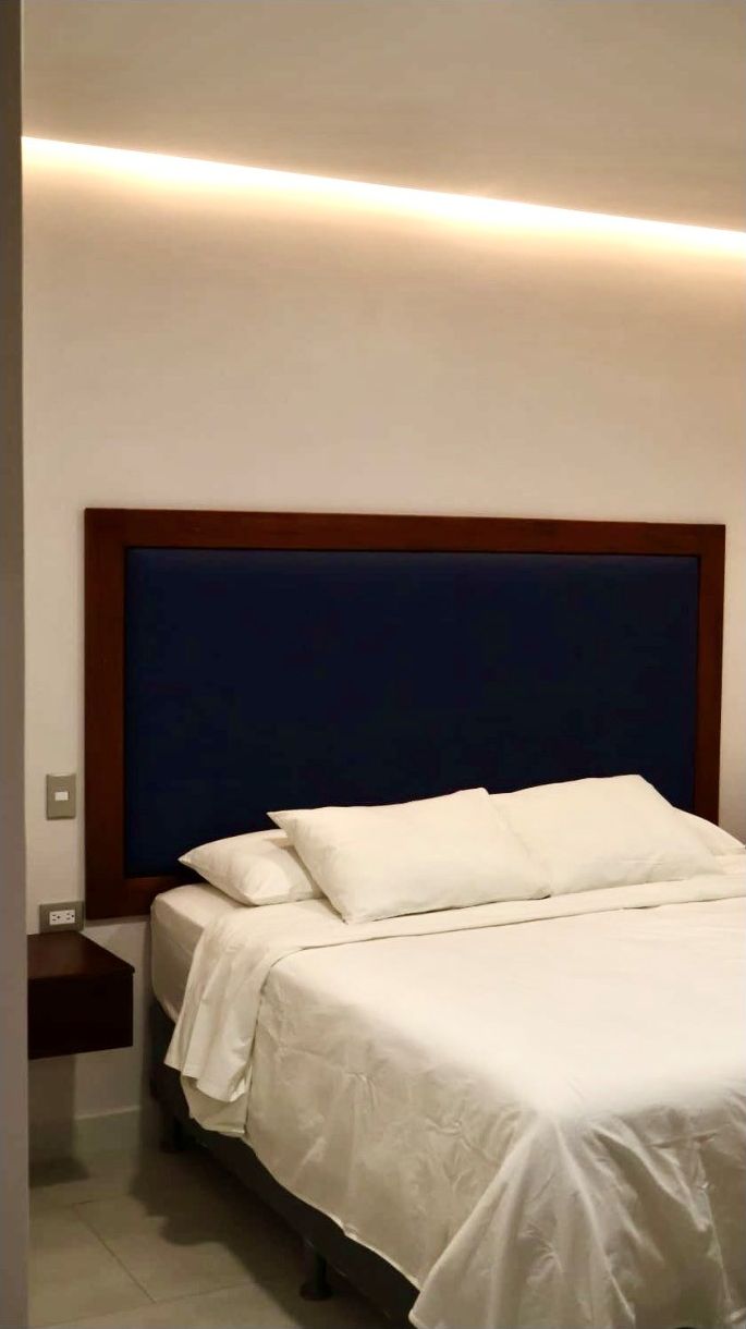 Una habitación de hotel con una cama, una mesita de noche y una lámpara fijada a la pared.