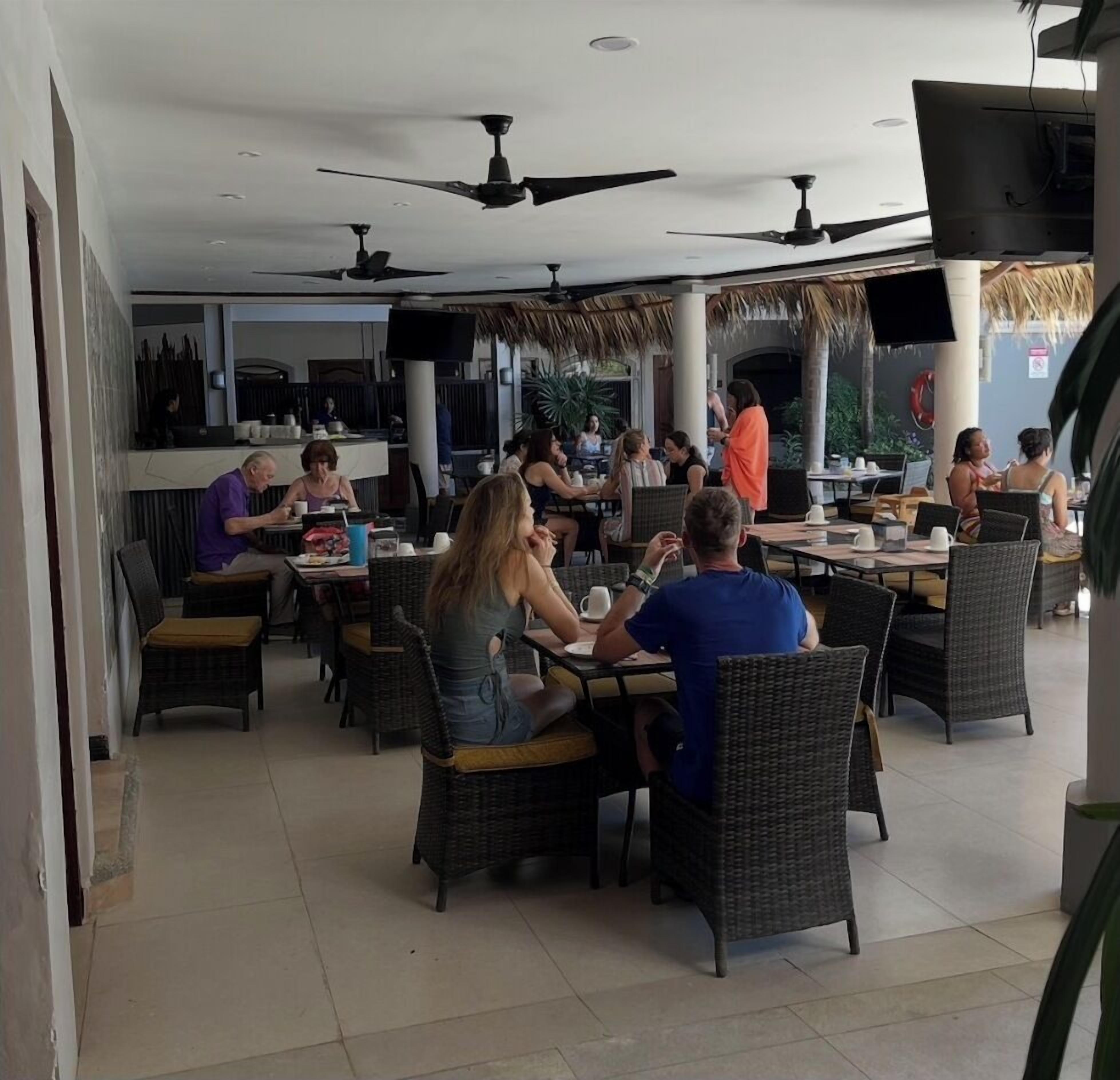 Ein Restaurant mit Terrassensitzgelegenheiten, Deckenventilatoren und einem Reetdach.