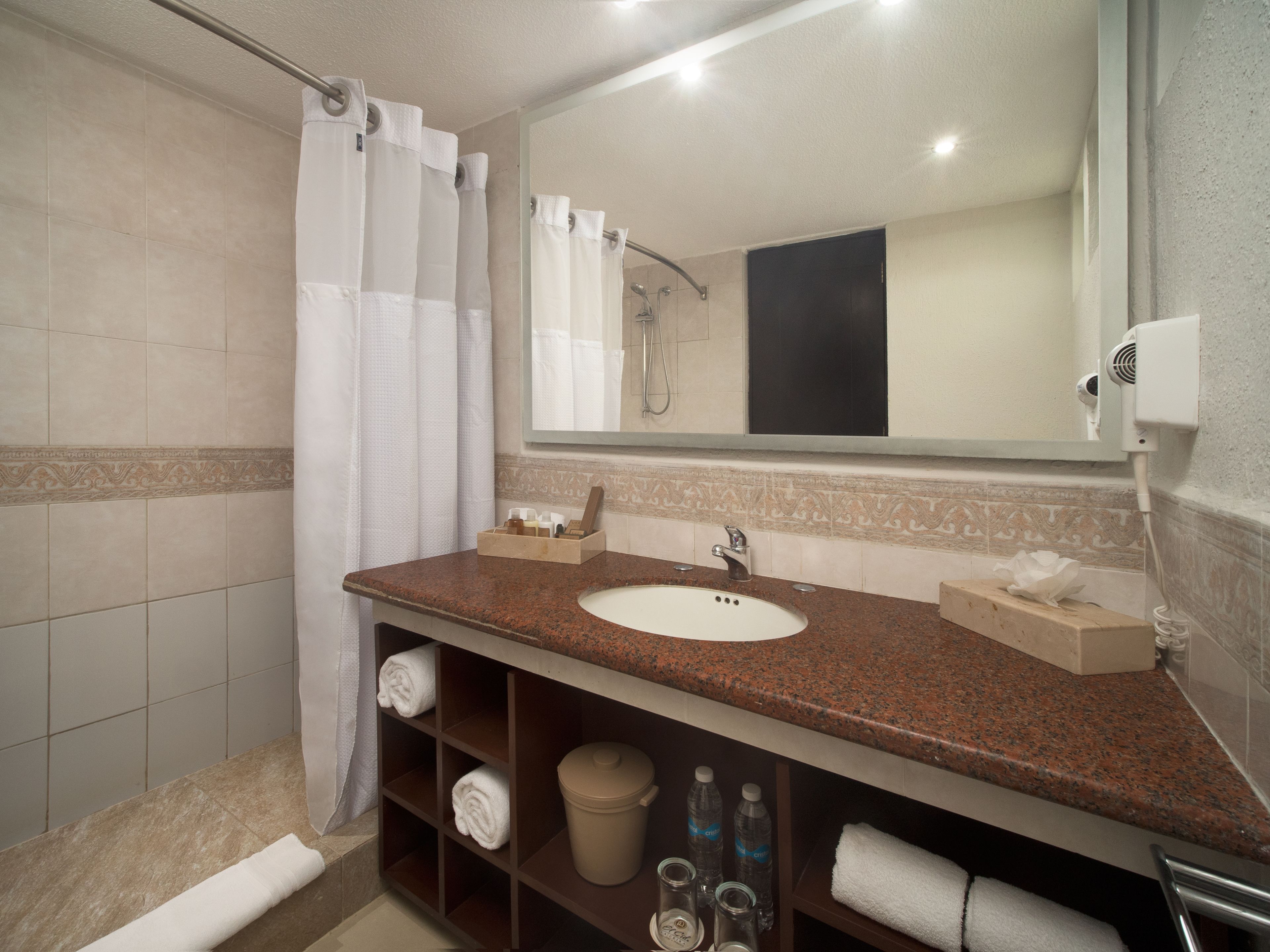 A bathroom with a sink, mirror, shower, and towel rack.