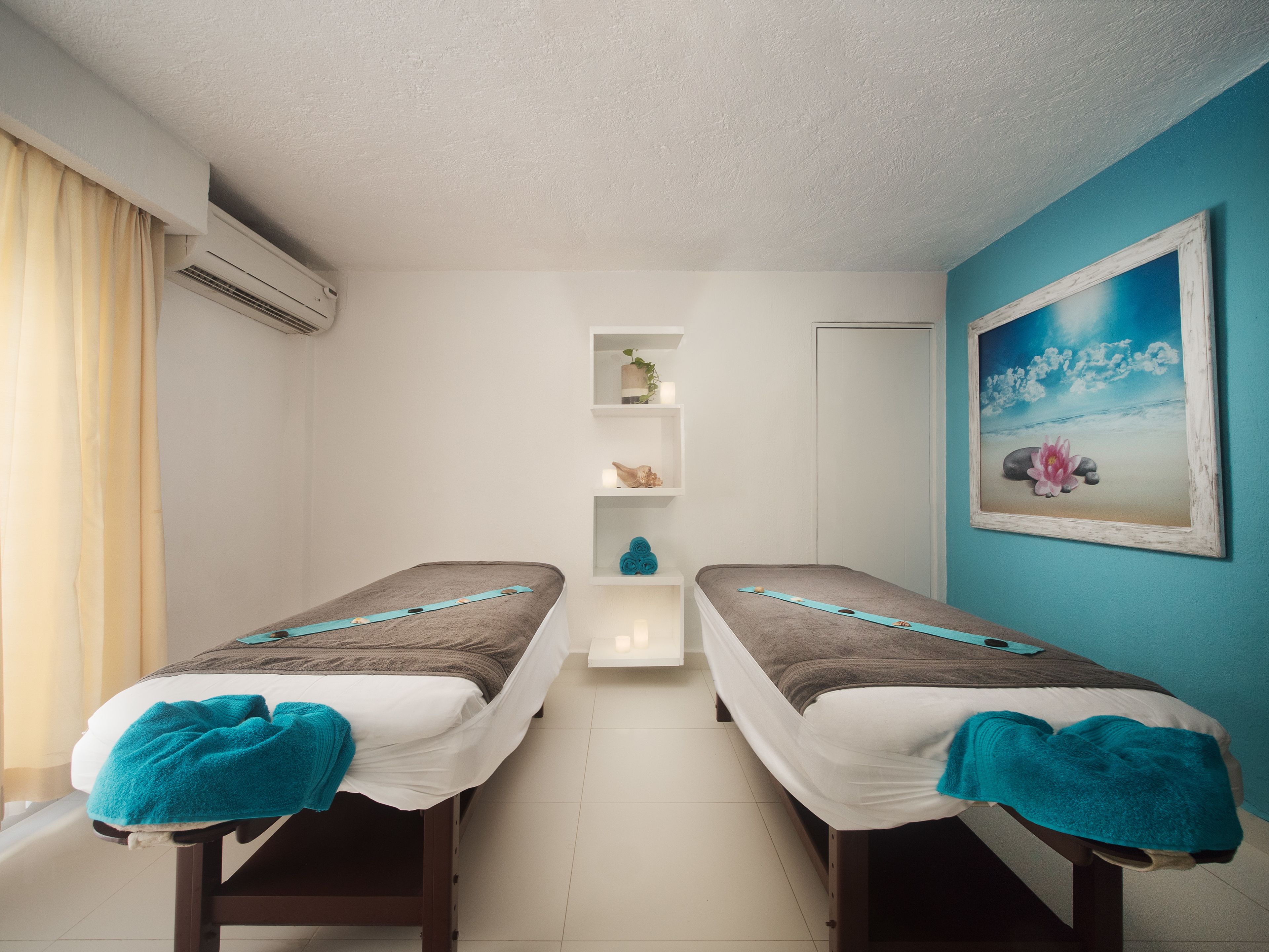 Ein Zimmer mit zwei Einzelbetten, einer kleinen Regalkonstruktion mit Dekoration, einem Gemälde mit Strandmotiv und einer Klimaanlage.