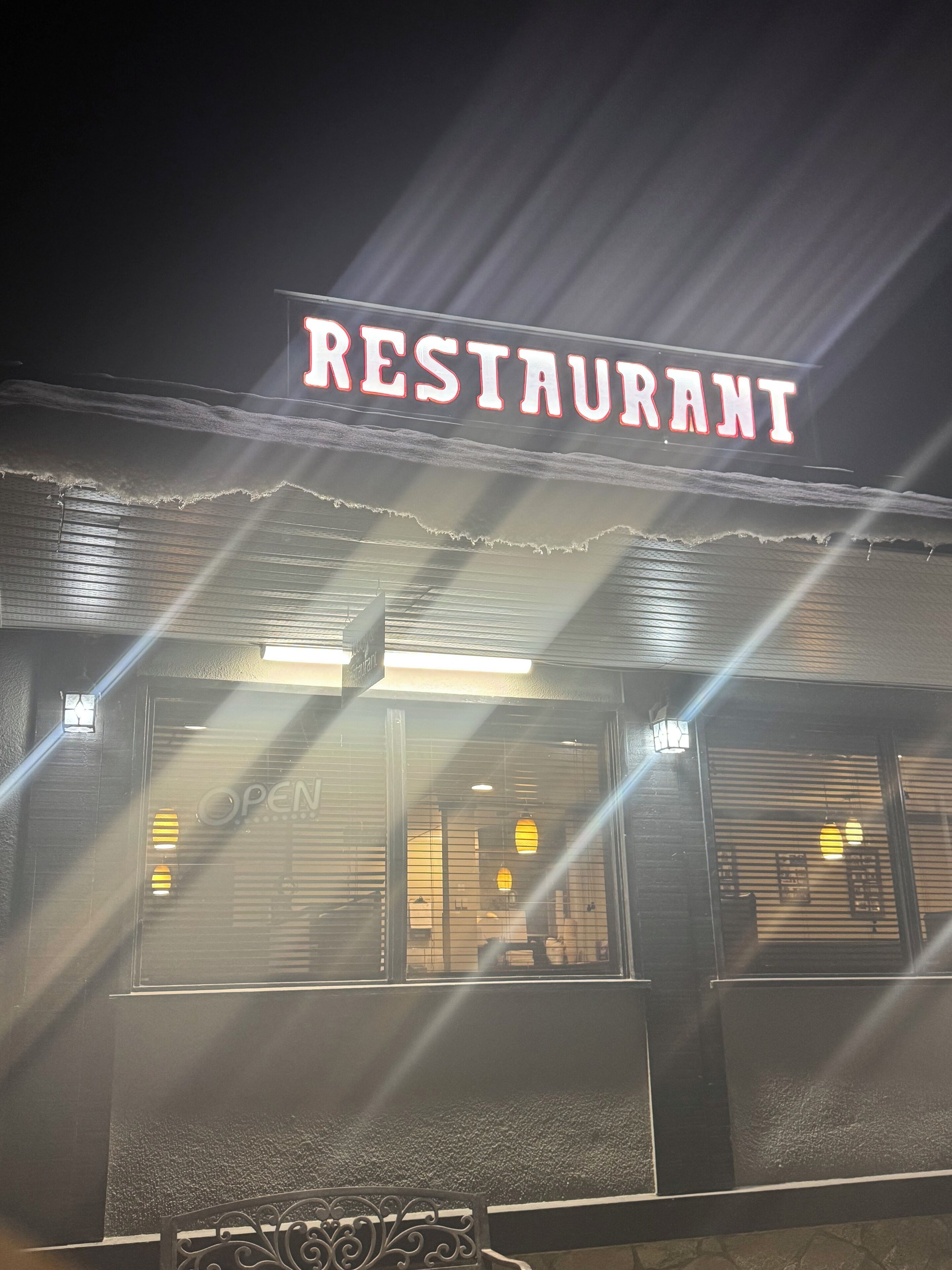 Un restaurante con un letrero de neón, una persiana cerrada y una barandilla metálica decorativa al frente.