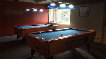 Two pool tables in a room with red walls, a window with a view, and a ceiling fan.