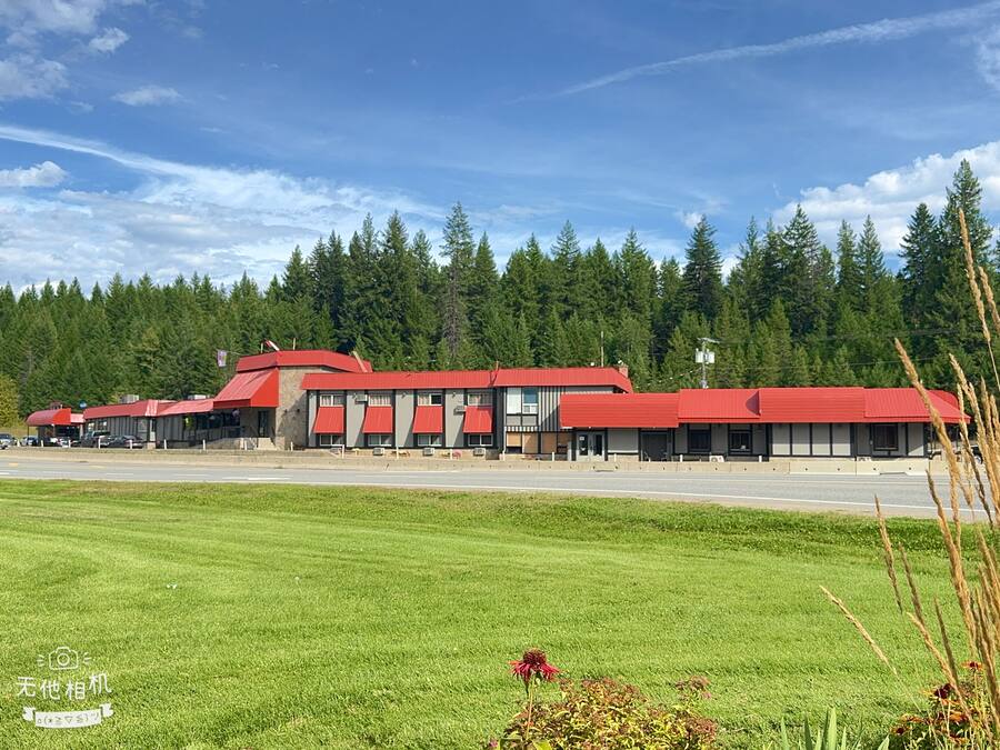 A hotel with a red roof and multiple buildings, surrounded by a green field and a forest.