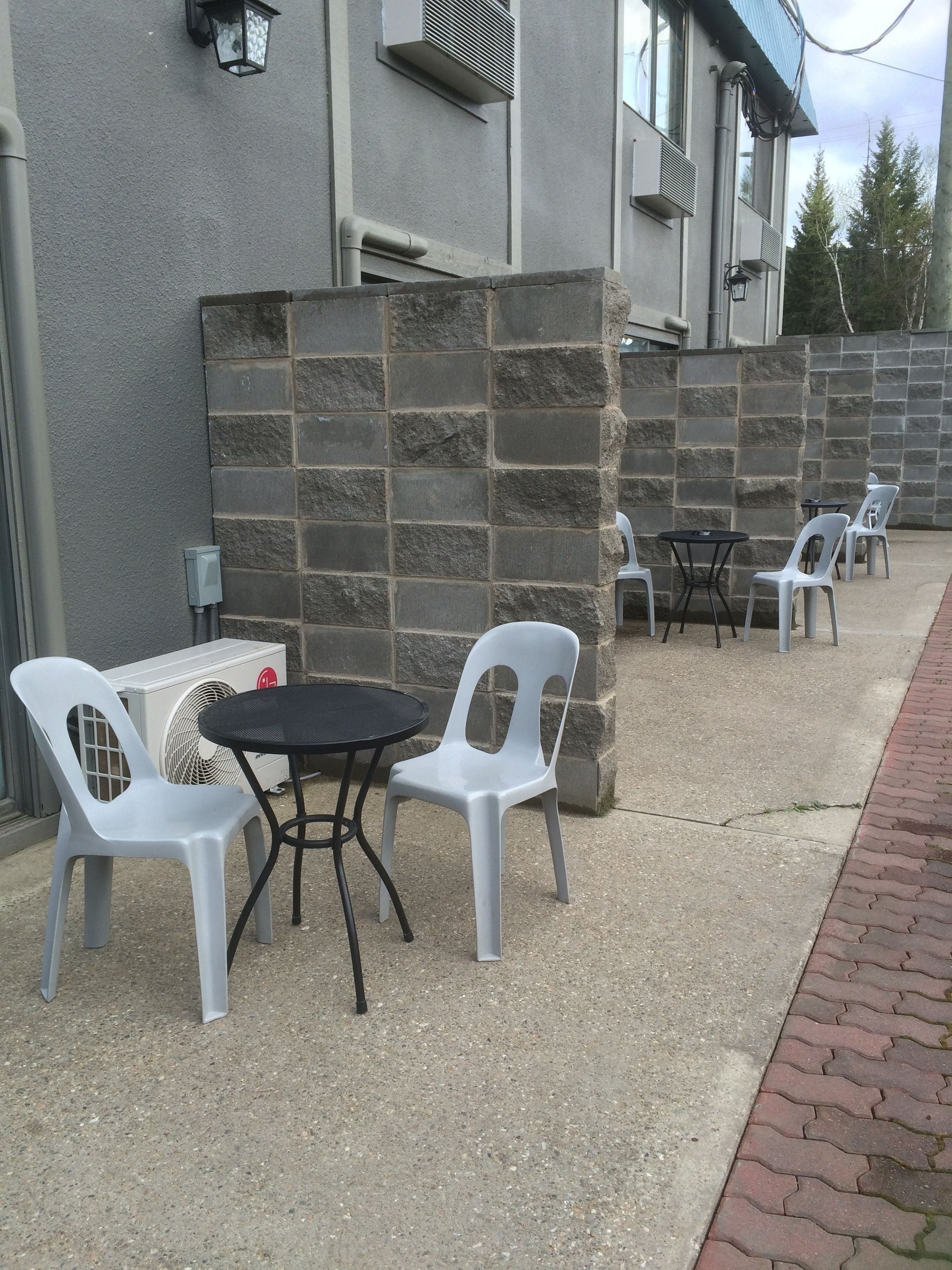 Un espace extérieur aménagé avec des chaises en plastique blanches et une table ronde, un mur en pierre et un appareil de climatisation.