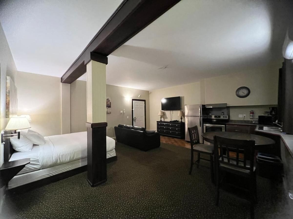 A compact hotel room with a bed, a desk, a chair, a television, and a kitchenette.