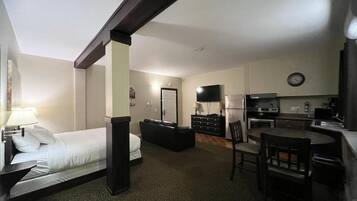 A compact hotel room with a bed, a desk, a chair, a television, and a kitchenette.