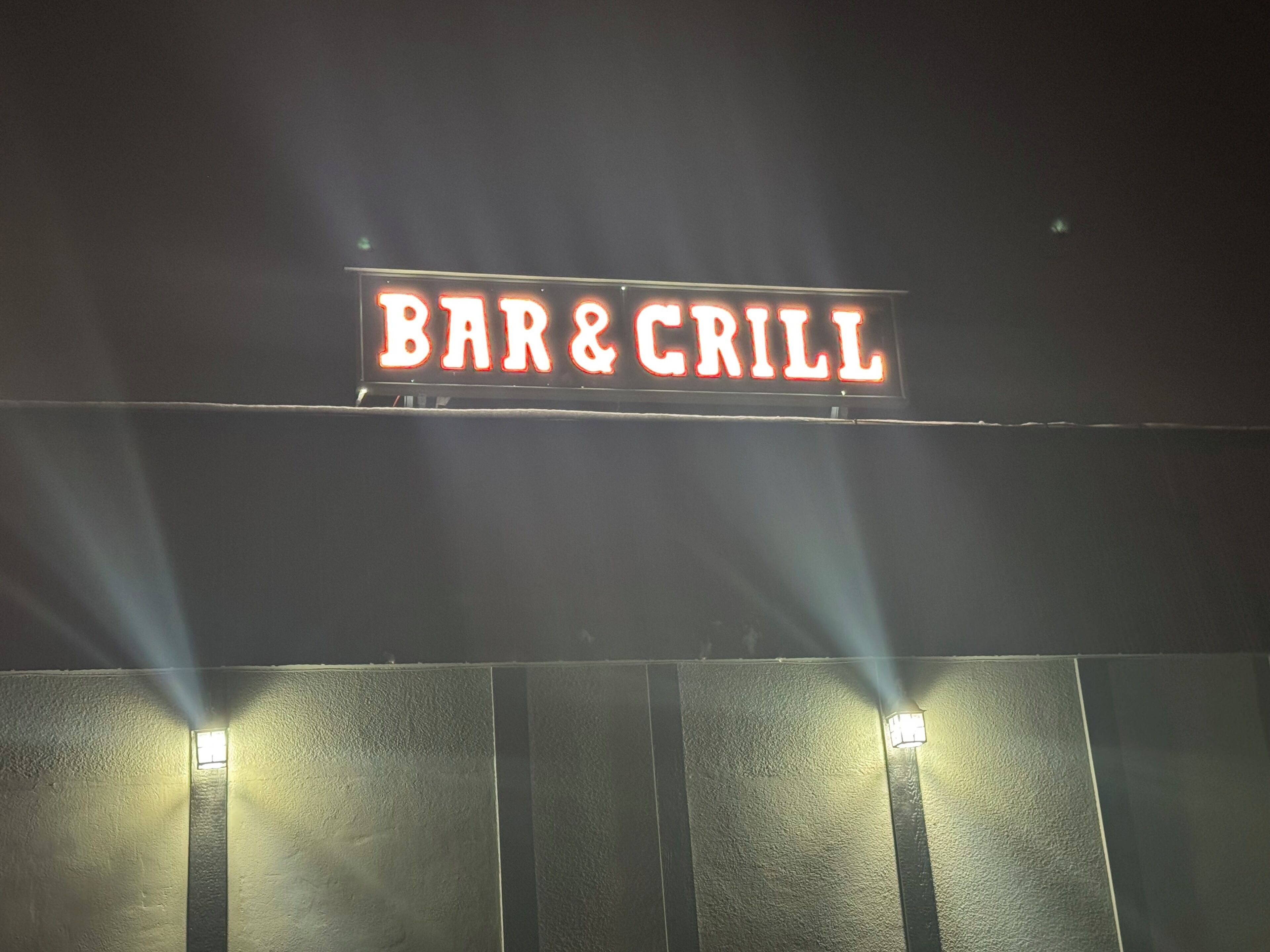 Une enseigne avec les mots « BAR & GRILL » illuminés en rouge.