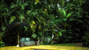 A pool area with a blue-tiled edge, surrounded by lush greenery and a wicker sofa with an umbrella. - Monoceros Resort (Mae Rim)