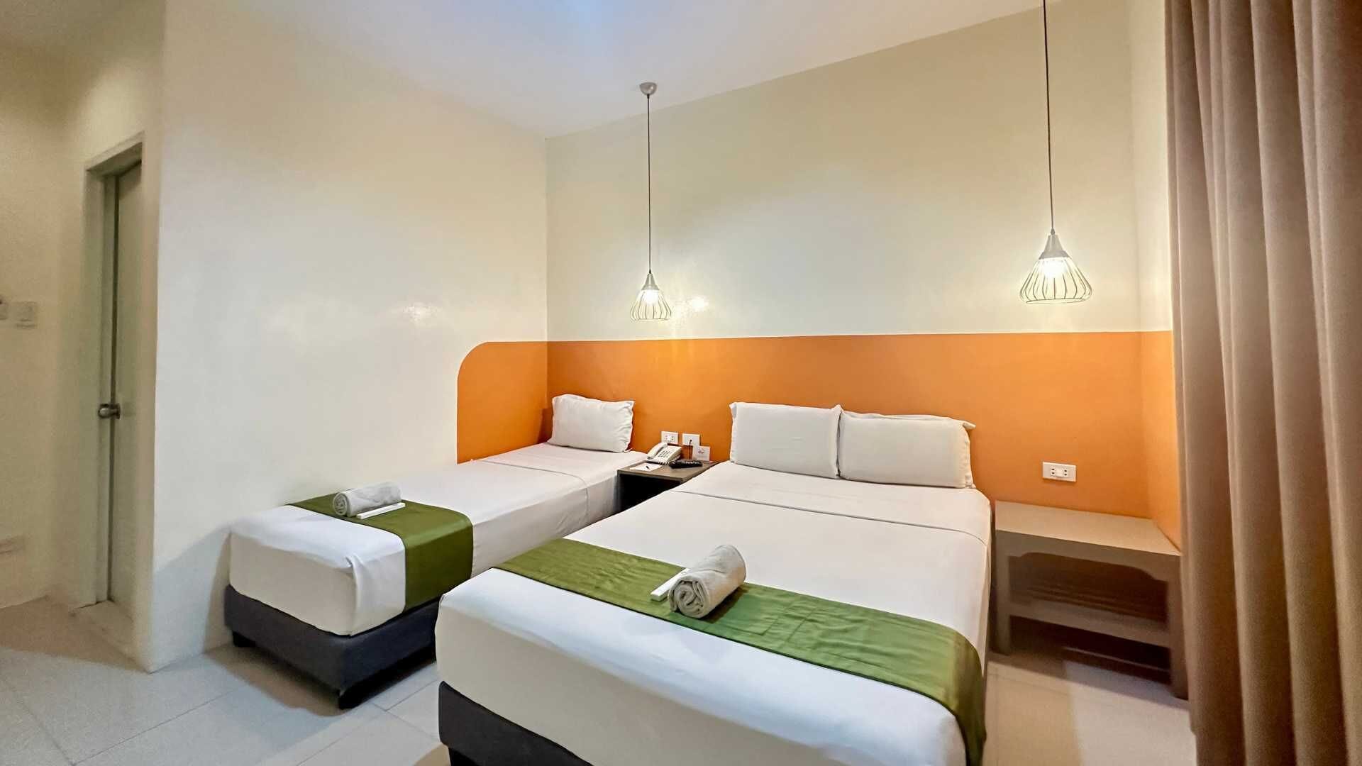 Een hotelkamer met twee eenpersoonsbedden, een nachtkastje met telefoon, en een deur links.