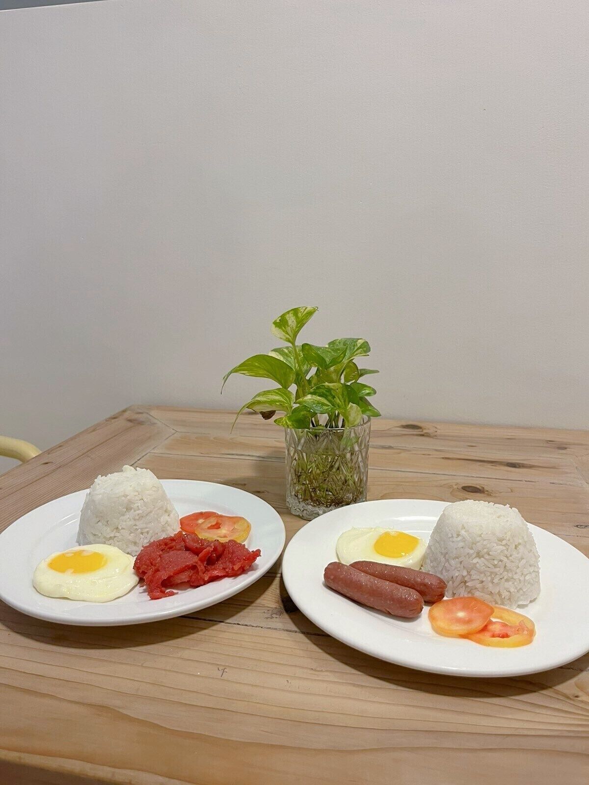 Duas travessas de comida com arroz, ovos, tomate e carne sobre uma mesa de madeira.