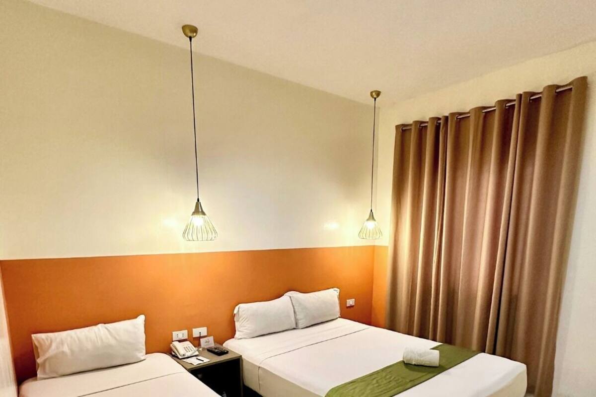 Une chambre d’hôtel avec deux lits, chacun recouvert d’une couverture verte et doté d’oreillers blancs, ainsi qu’un téléphone et une table de chevet.