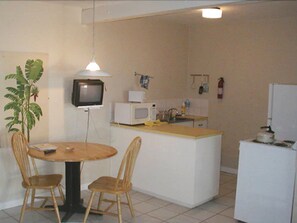 A compact kitchen with a dining table, two chairs, a microwave, a small refrigerator, and a television. - Paradise Villas (Bridgetown)