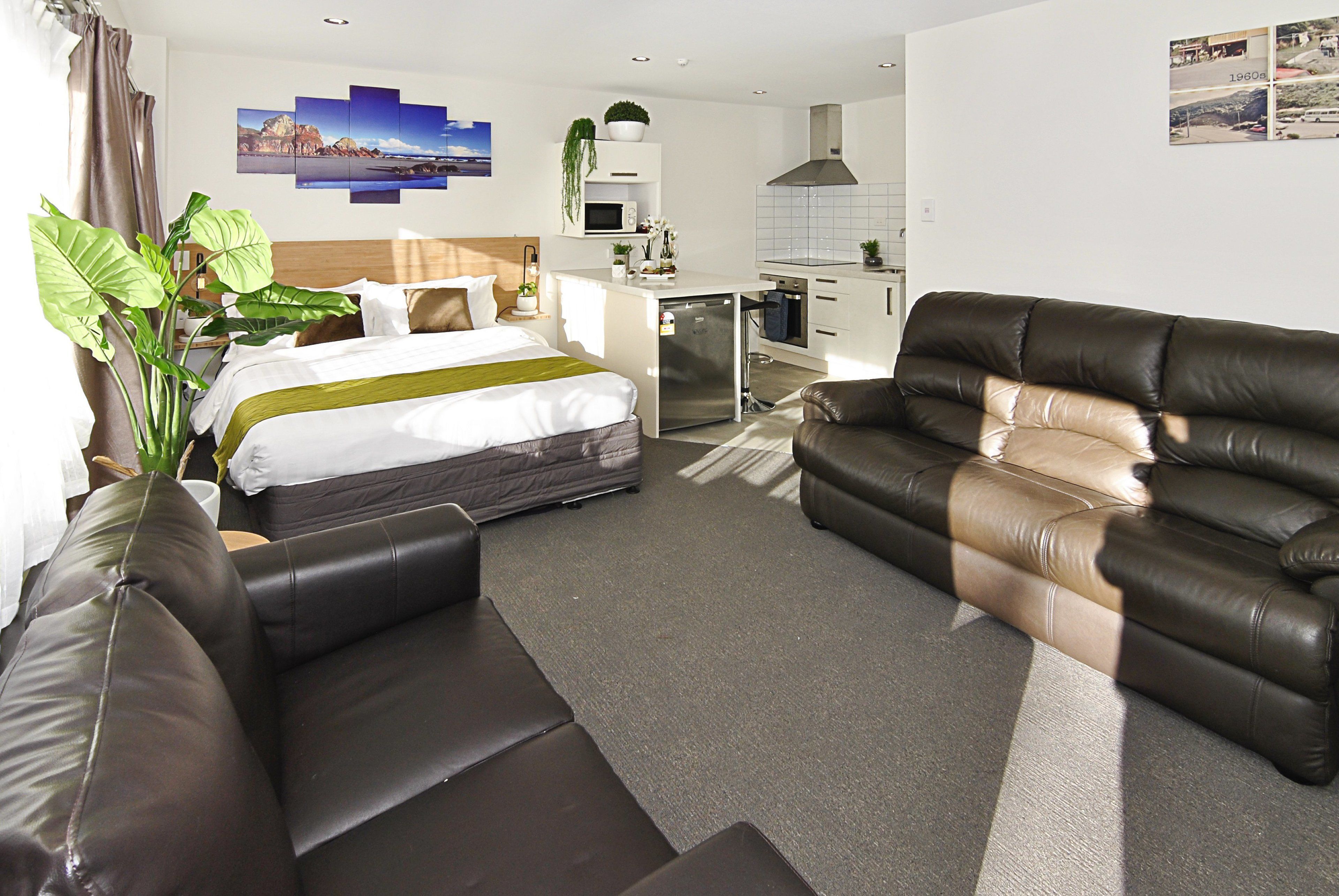Una habitación de hotel moderna con una cama, un sofá de cuero, una pequeña cocina y un amplio ventanal.