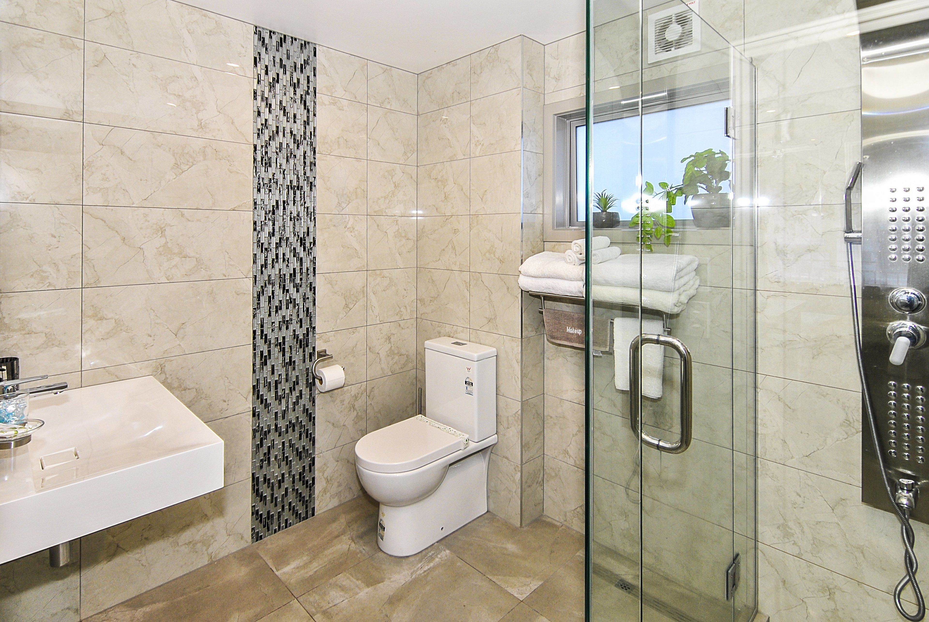 Un baño moderno con cabina de ducha de vidrio, un lavamanos blanco y un inodoro.