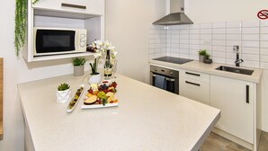 A modern kitchen with white cabinets, a microwave, a sink, and a countertop with a fruit and cheese board. - Newlands Court Motel (Wellington)