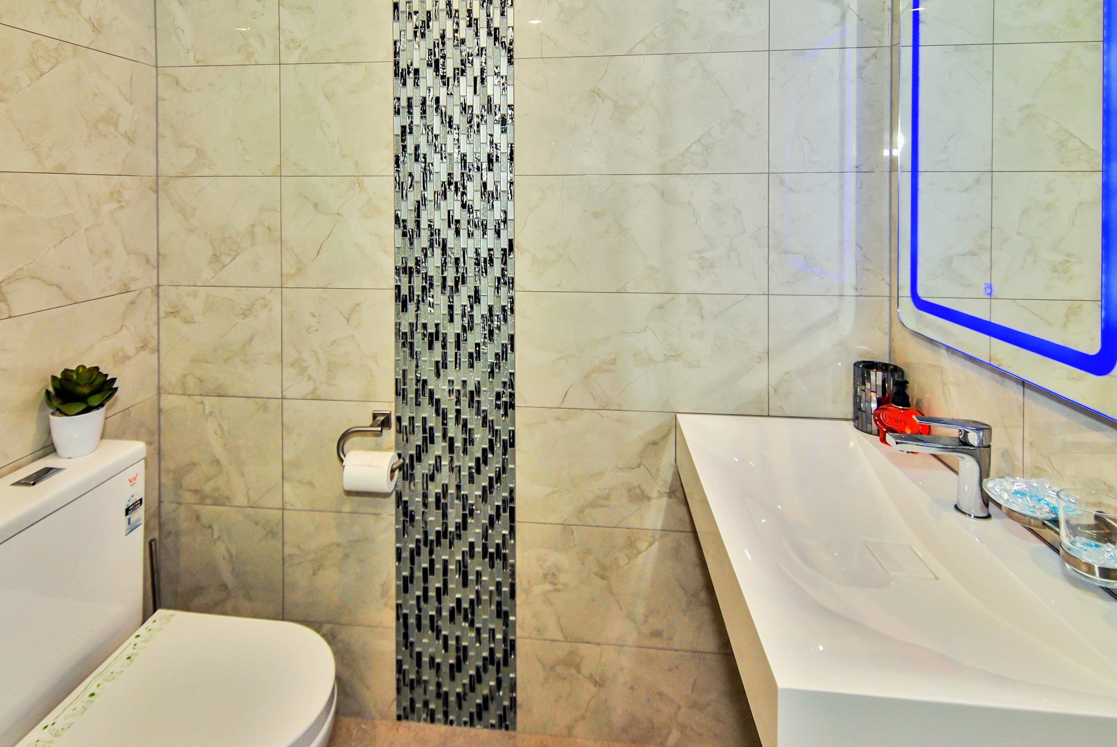 Un baño con inodoro blanco, lavabo con espejo y un zócalo vertical estampado en la pared.