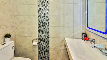 Un baño con inodoro blanco, lavabo con espejo y un zócalo vertical estampado en la pared.