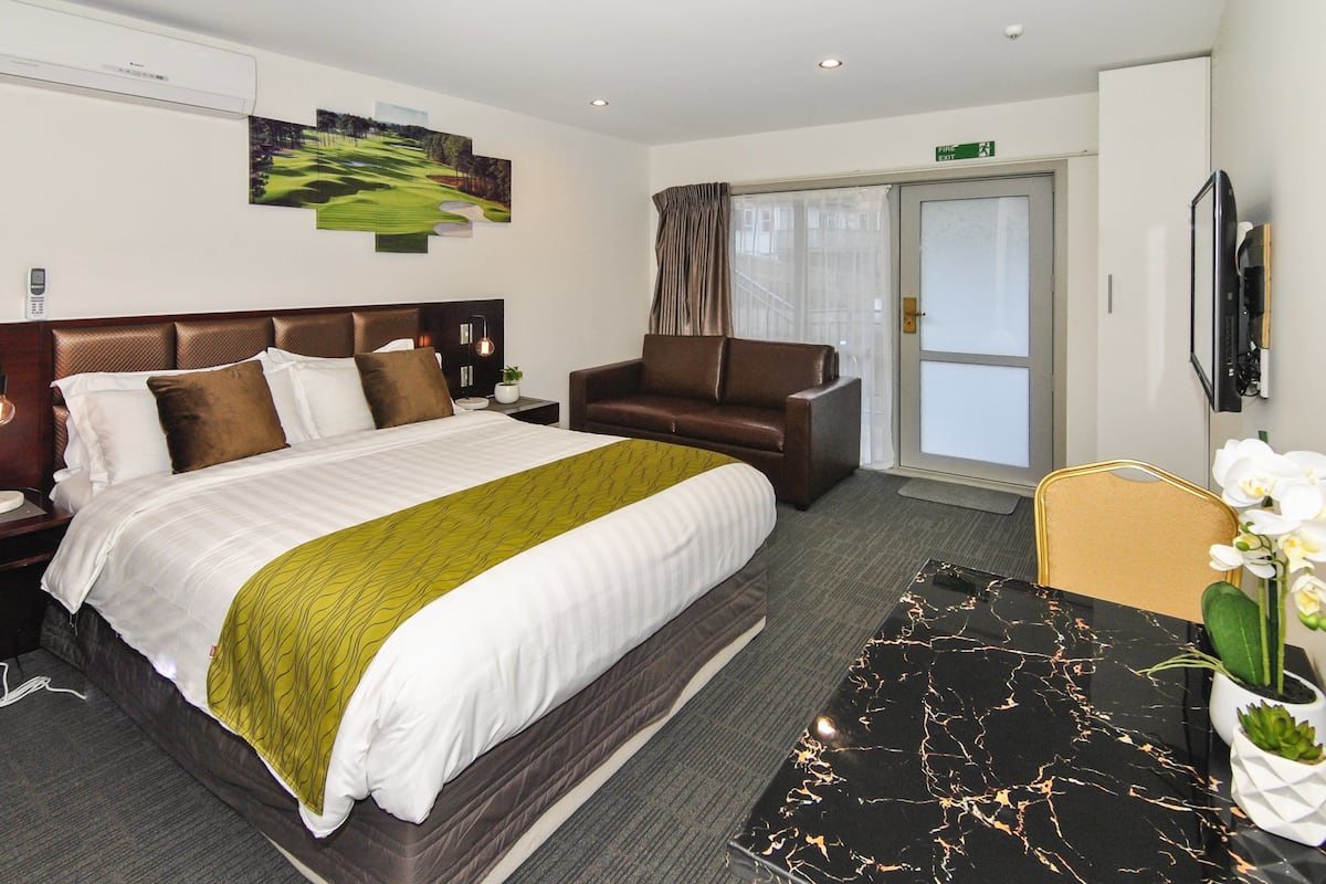 A hotel room with a large bed, a sofa, a dining table, and a TV.