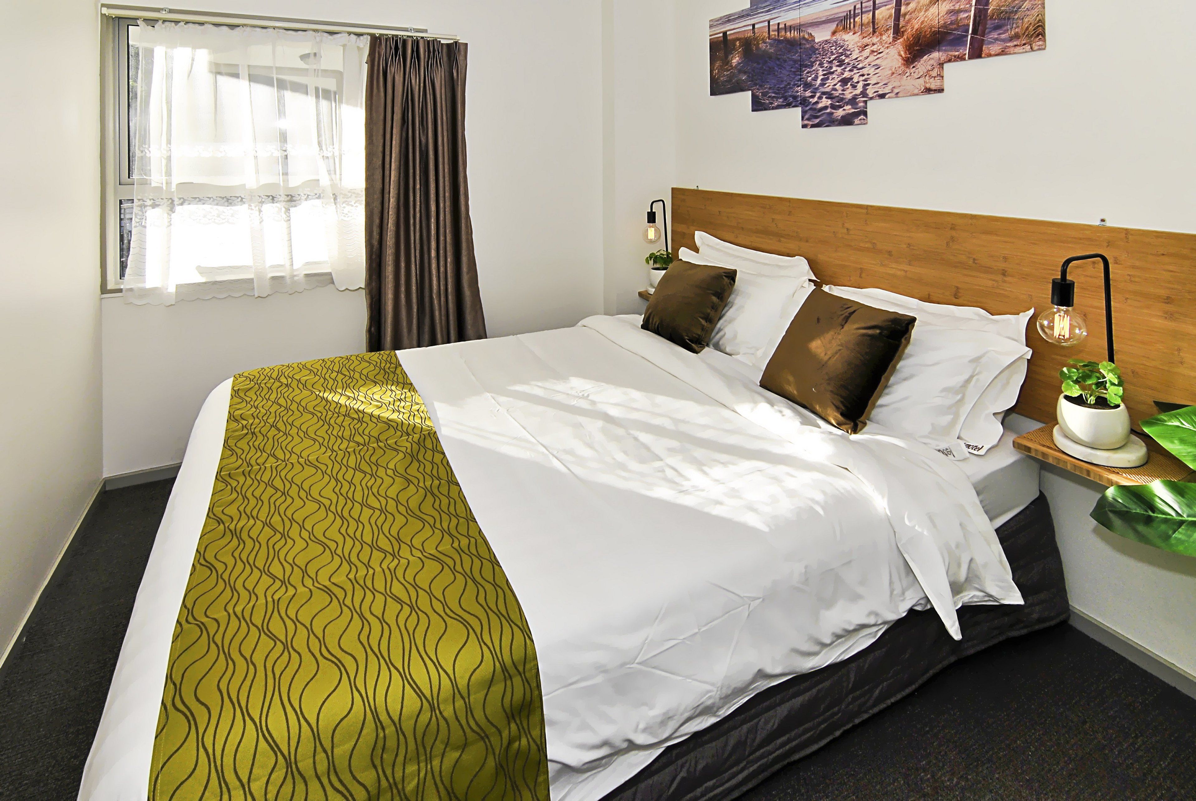 A neatly made bed with a patterned bedspread, a wooden headboard, and a nightstand with a lamp and a potted plant.