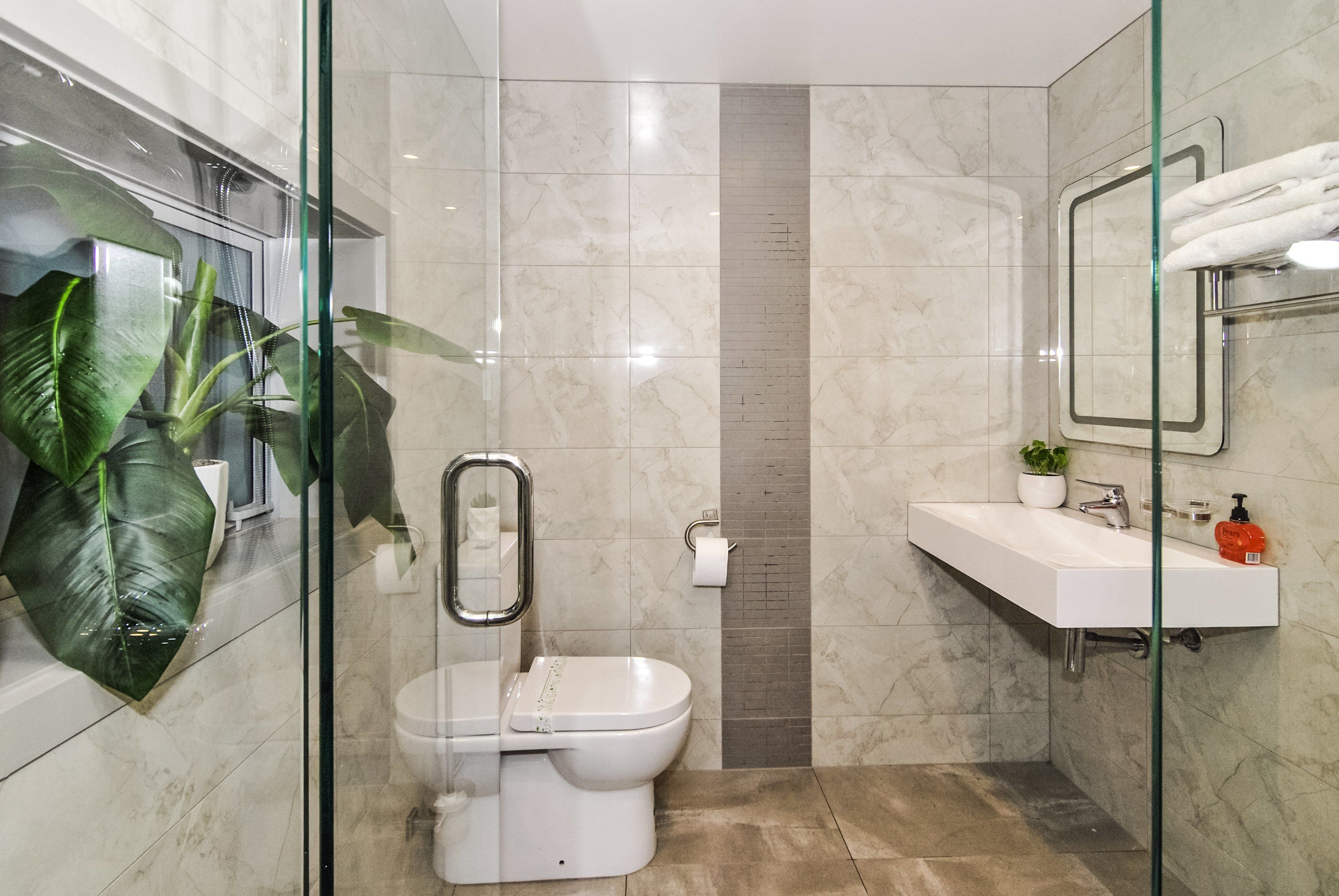 A modern bathroom with a glass shower enclosure, a white toilet, a sink with a mirror, and a potted plant.