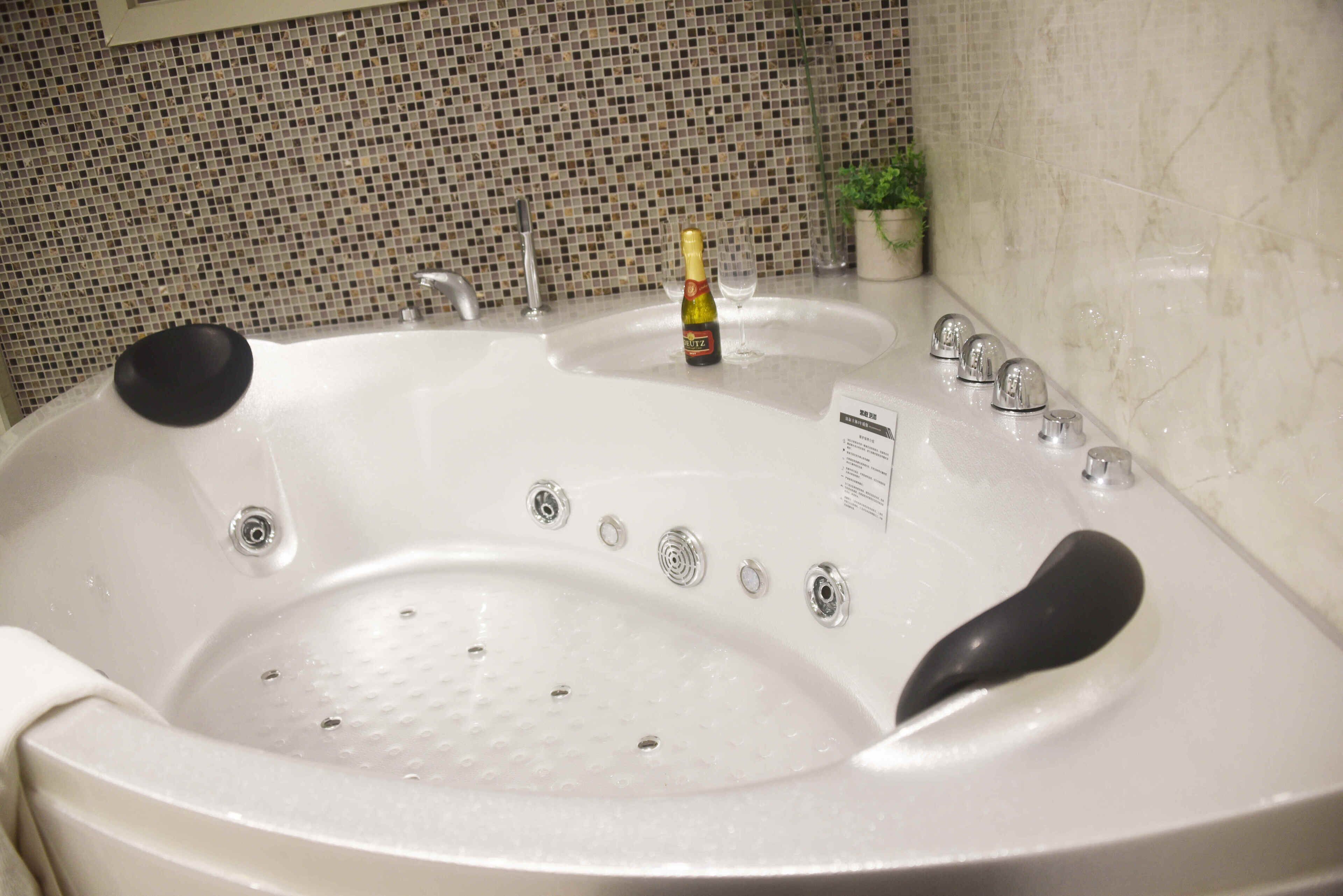 A large, white bathtub with a bottle of champagne and a glass, surrounded by a tiled mosaic wall.