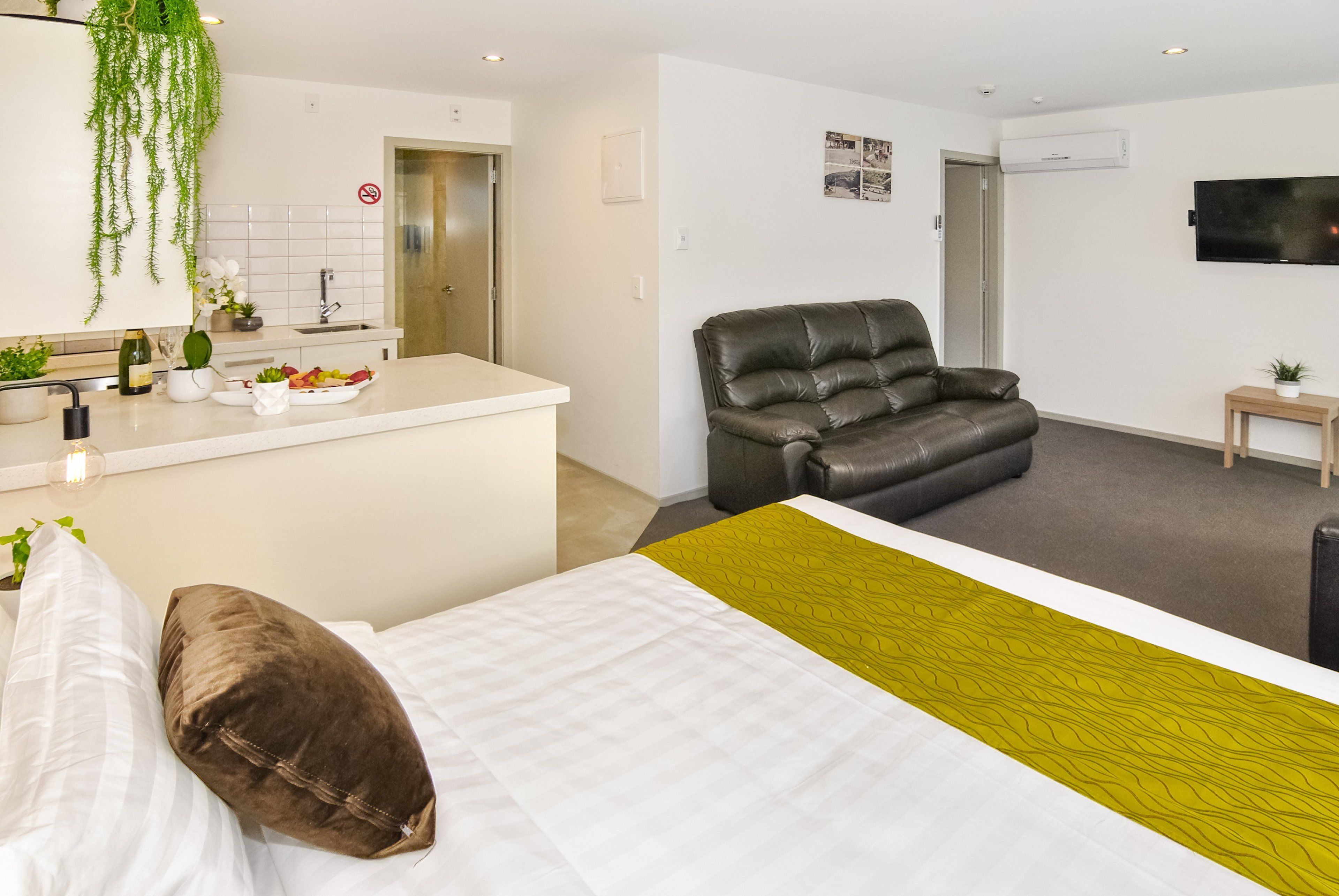 A modern hotel room with a bed, a sofa, a dining area, and a TV.