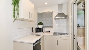 A compact kitchen with white cabinets, a microwave, a sink, and a stove. - Newlands Court Motel (Wellington)