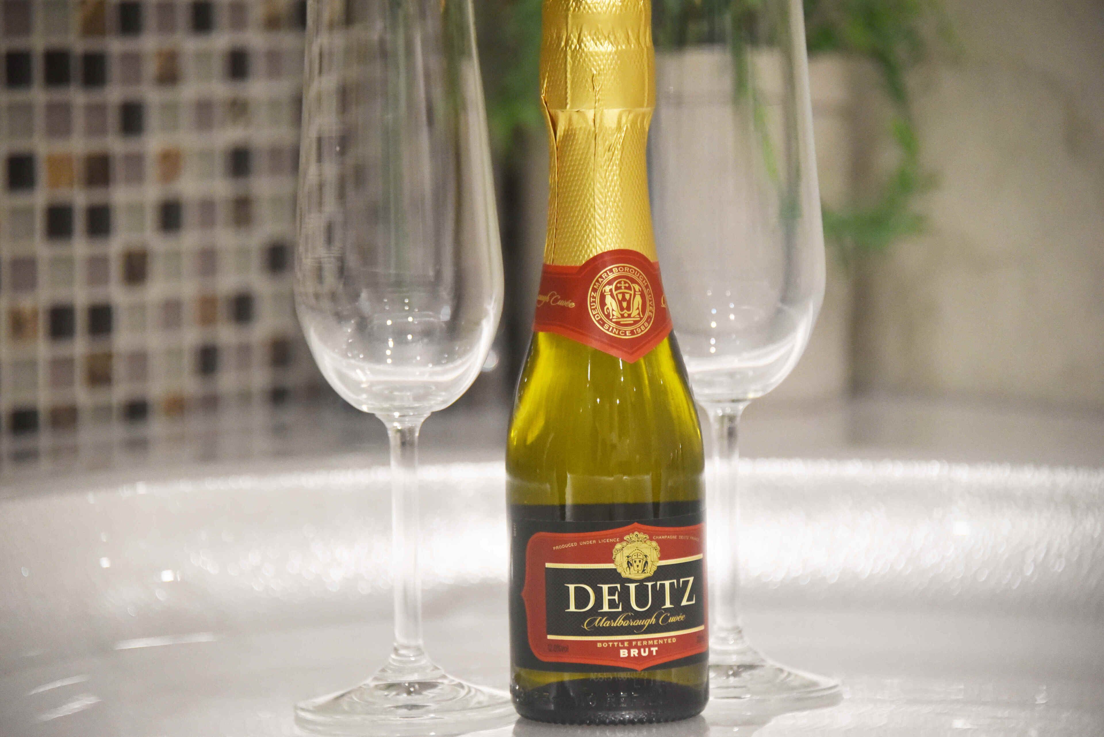Una botella de vino Deutz Brut y dos copas de vino vacías sobre una mesa.