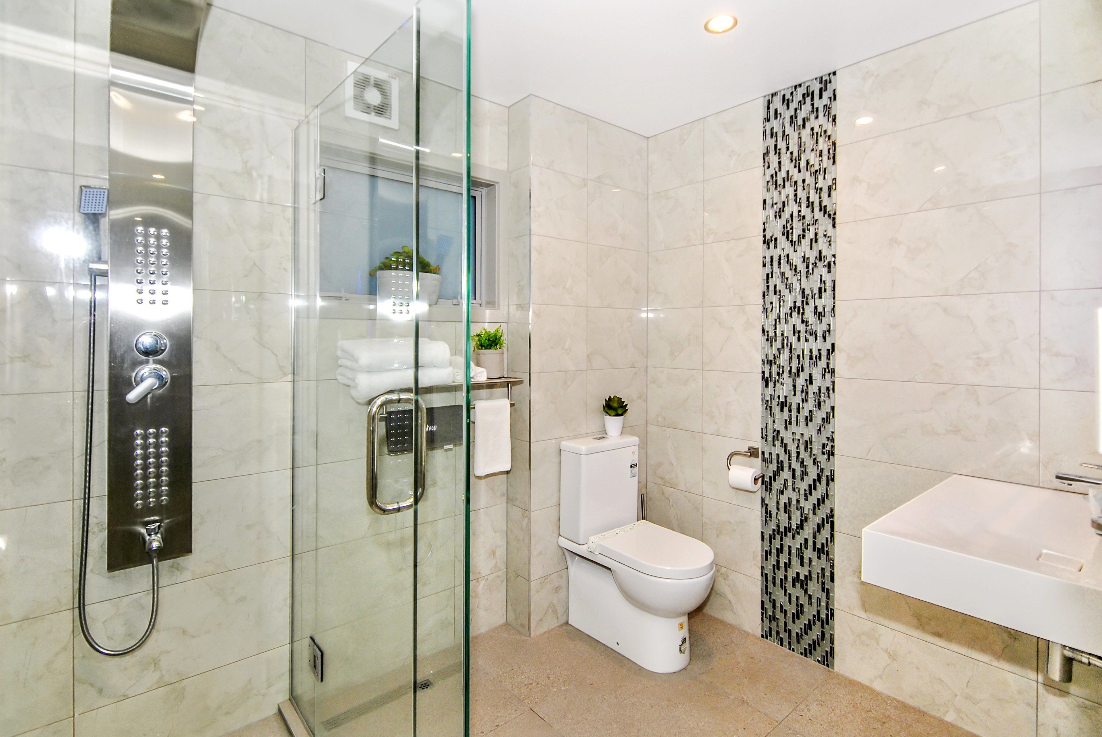 A modern bathroom with a glass-enclosed shower, a white toilet, and a sink.