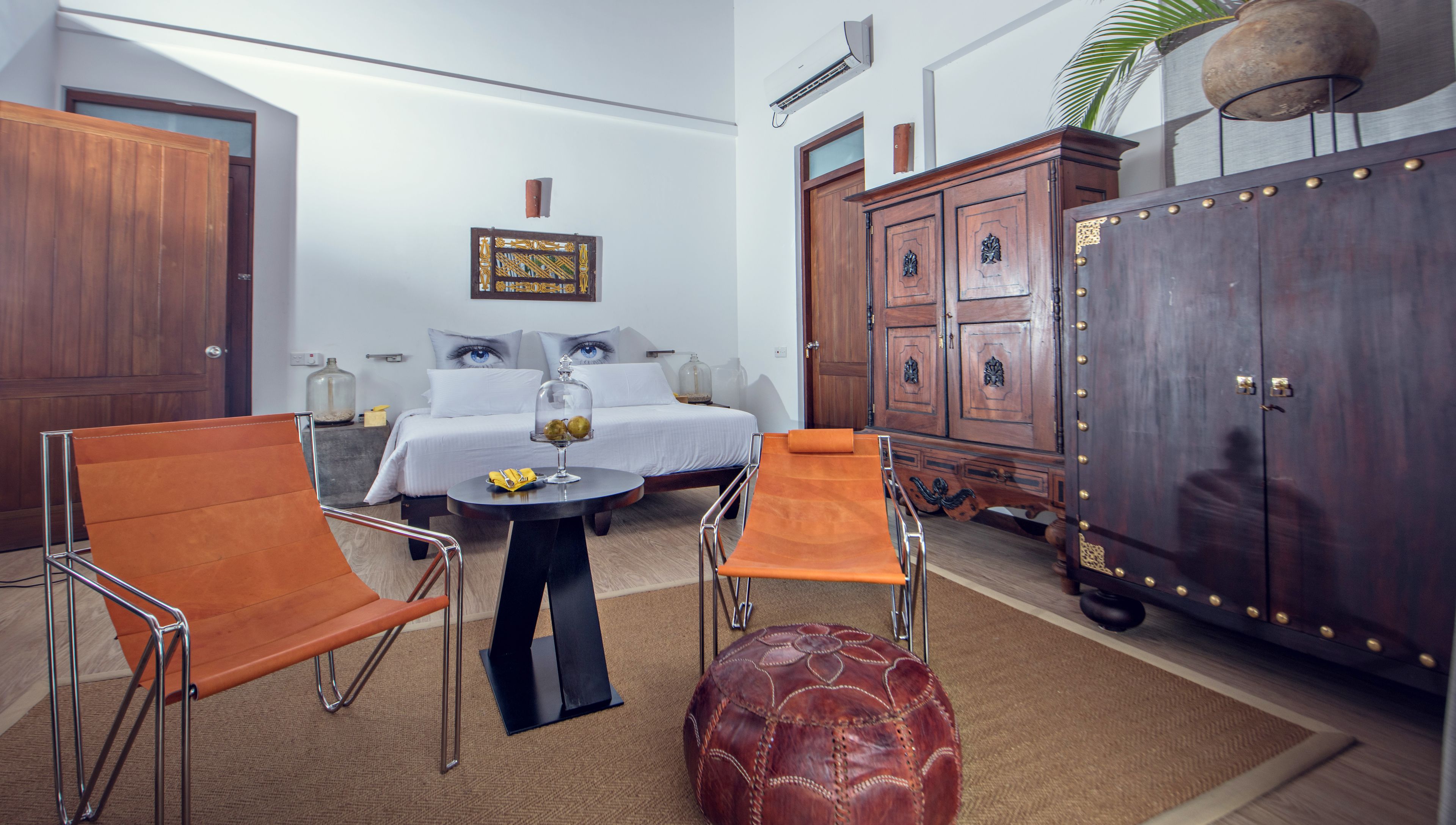 A modern hotel room with a bed, two armchairs, a small table, and a large wooden cabinet.