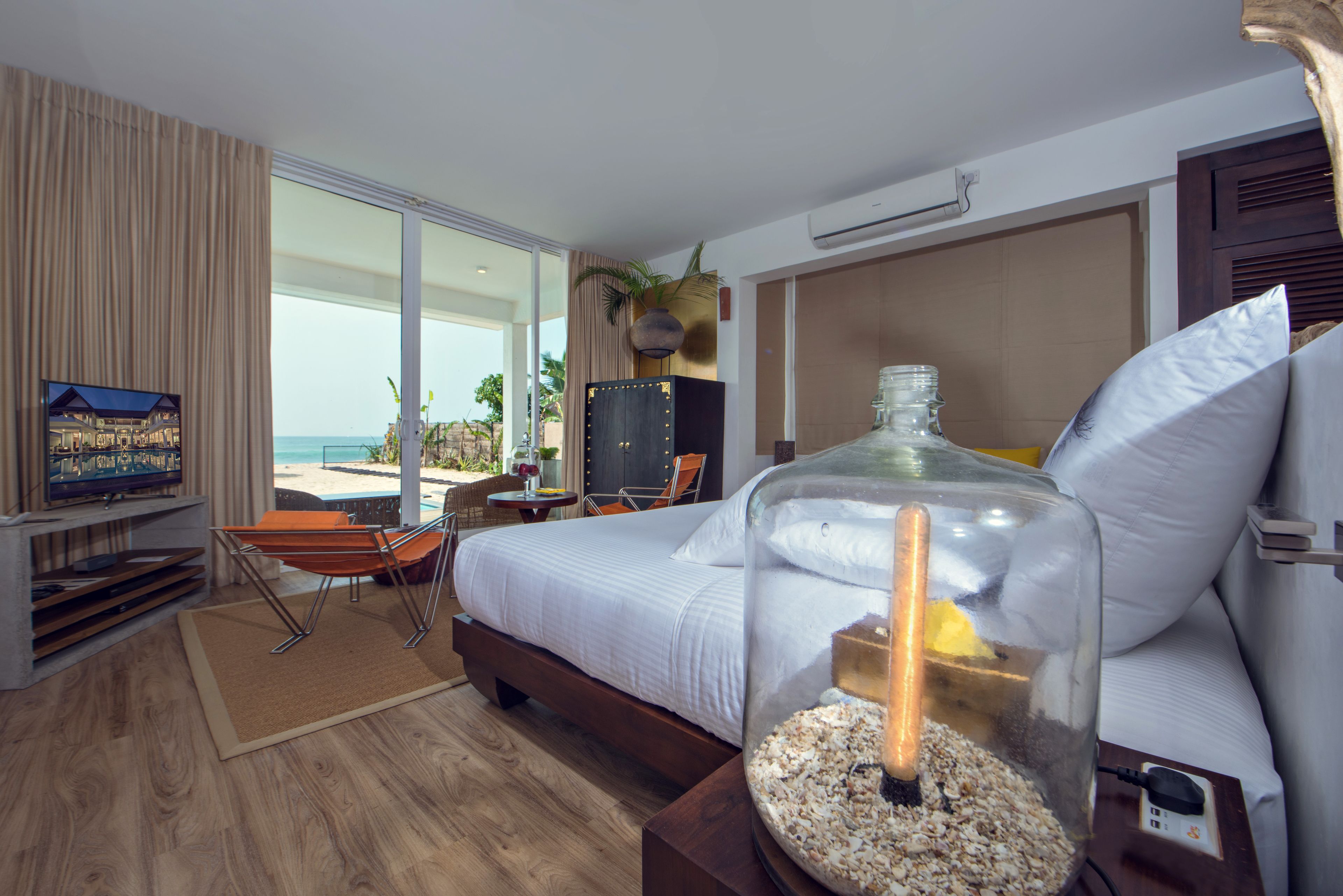 A hotel room with a bed, a glass fishbowl, a TV, and a view of the beach.