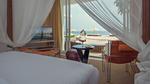 Une chambre d’hôtel avec un lit, une télévision, une table avec un verre et une vue sur la plage.