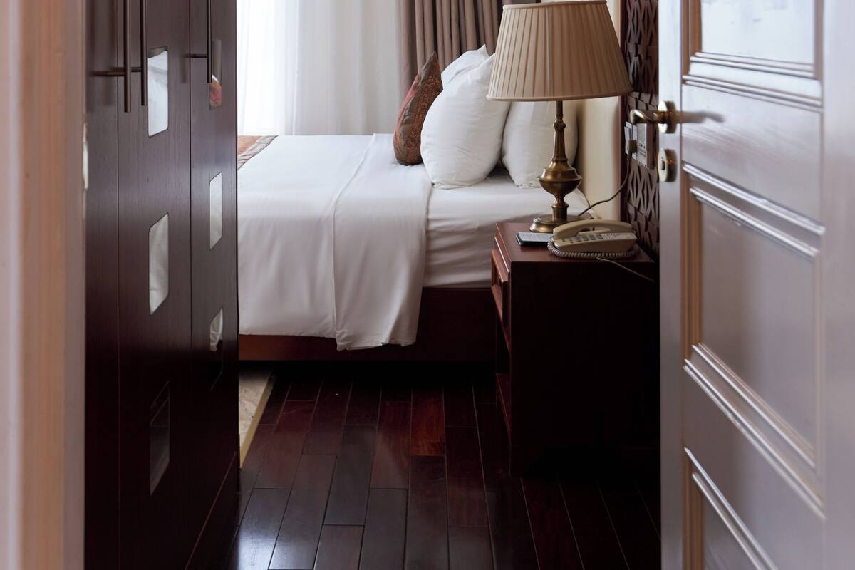 A hotel room with a bed, a bedside table with a lamp, a wardrobe, and a door with a decorative panel.