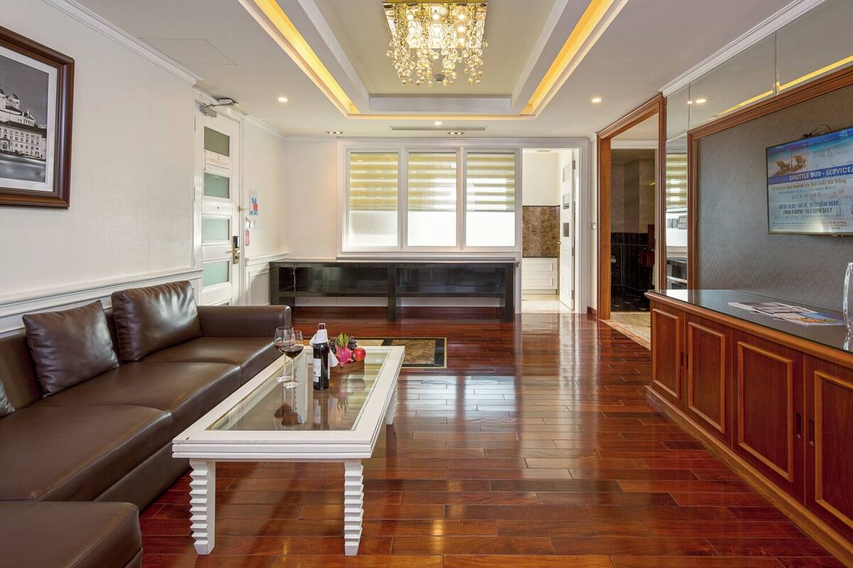 A spacious living area with a brown leather sofa, a glass coffee table, and a wooden reception desk.
