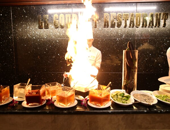 A chef performing a flambé with a lit torch in front of a sign that reads "Le Couvret Restaurant".