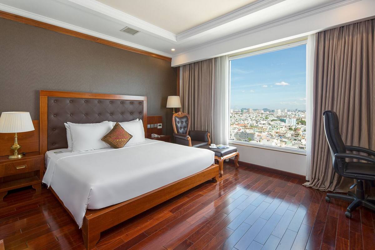 A hotel room with a large bed, a desk, a chair, and a view of the city.