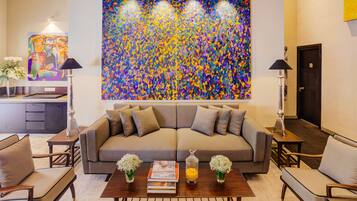 Una sala de estar con un cuadro abstracto grande, un sofá, sillones, una mesa de centro con libros y jarrones, y una lámpara.