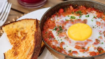 Ein Frühstücksteller mit Eiern und Tomaten, dazu ein Glas roter Saft und eine Scheibe Toastbrot.