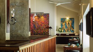 Un moderno vestíbulo de hotel con un mostrador de recepción de madera, un cuadro abstracto colorido y un área de comedor con mesas y sillas.