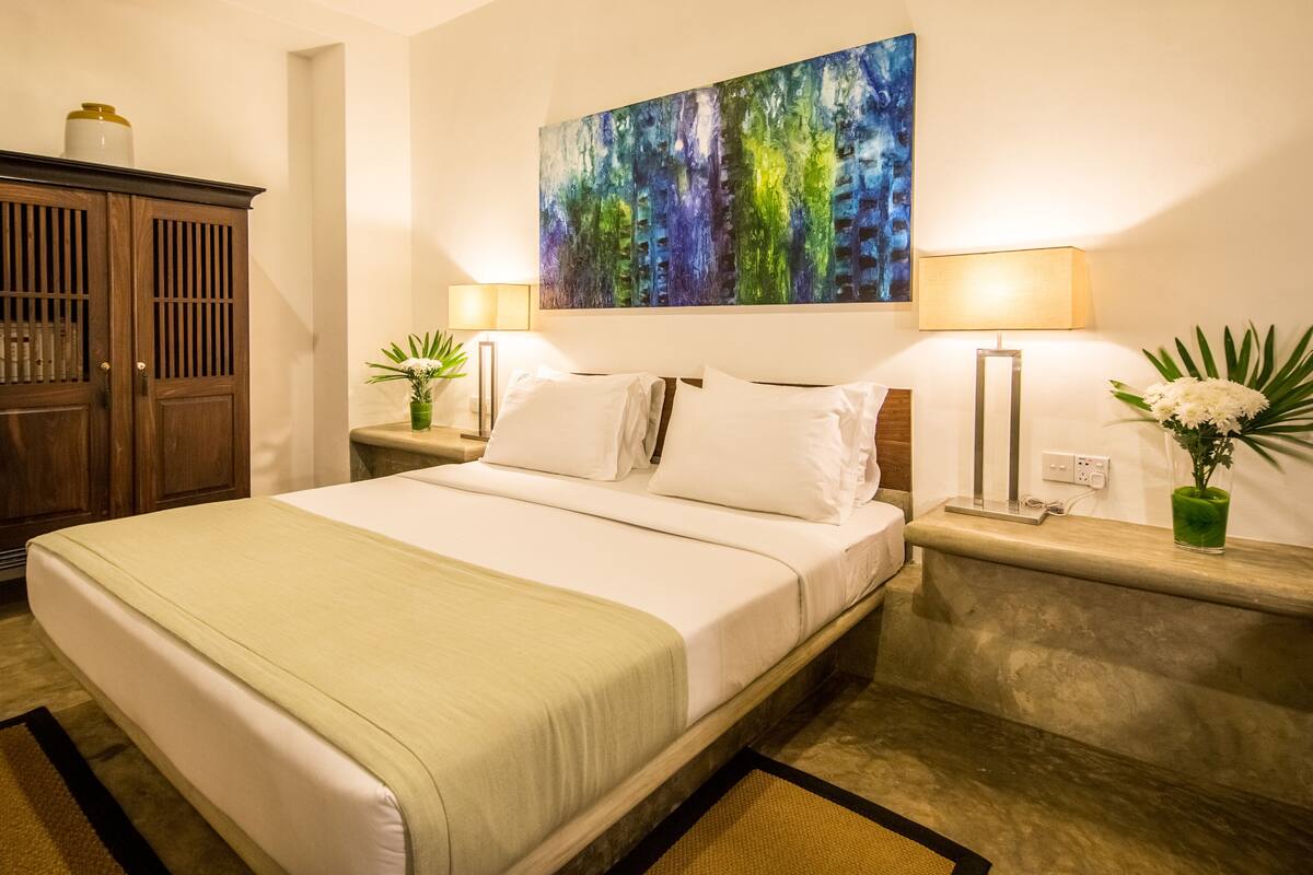 A neatly arranged hotel room with a bed, a wooden cabinet, a painting, and two bedside tables with lamps and vases.