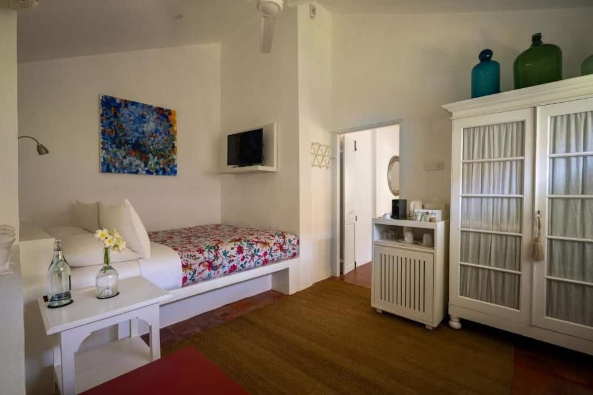 A bedroom with a bed, a white cabinet, a television, and a colorful painting on the wall.