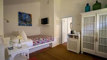 A bedroom with a bed, a white cabinet, a television, and a colorful painting on the wall.