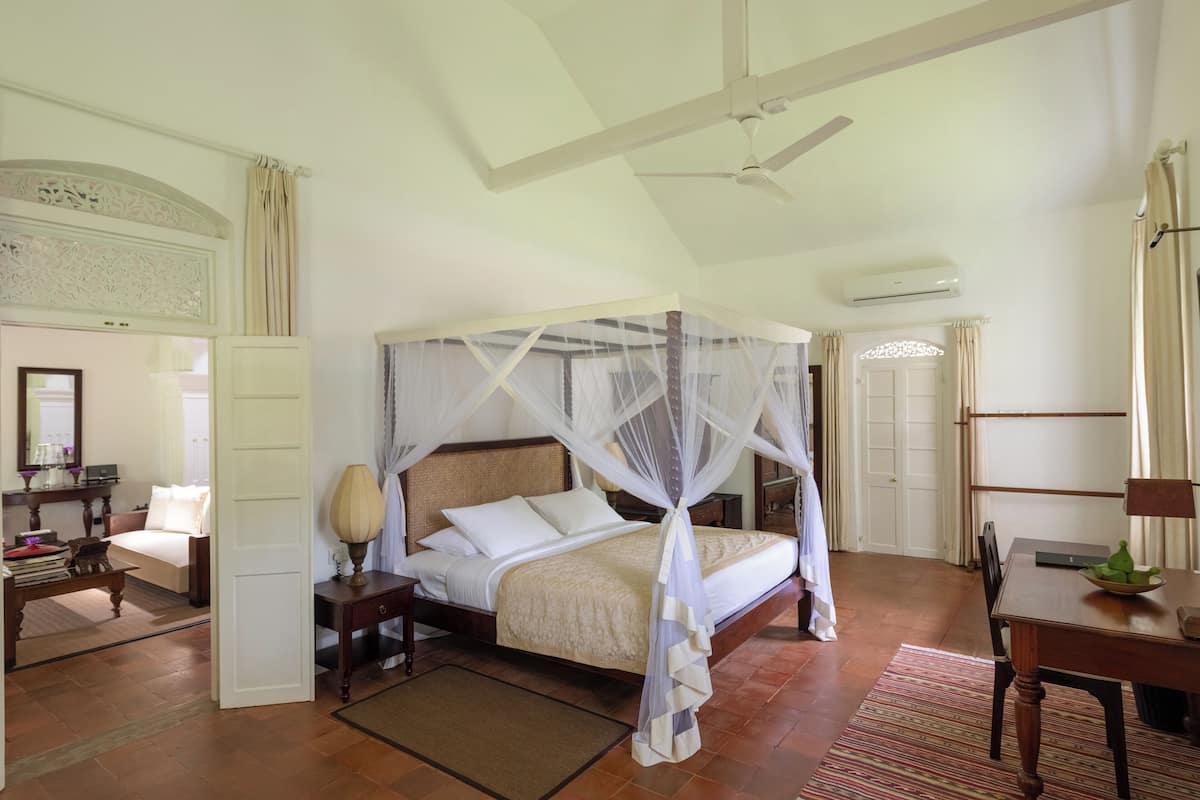 A spacious bedroom with a four-poster bed, a ceiling fan, and a dining area with a table and chairs.