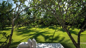 Una cama con almohadas en un exuberante jardín con árboles y césped.