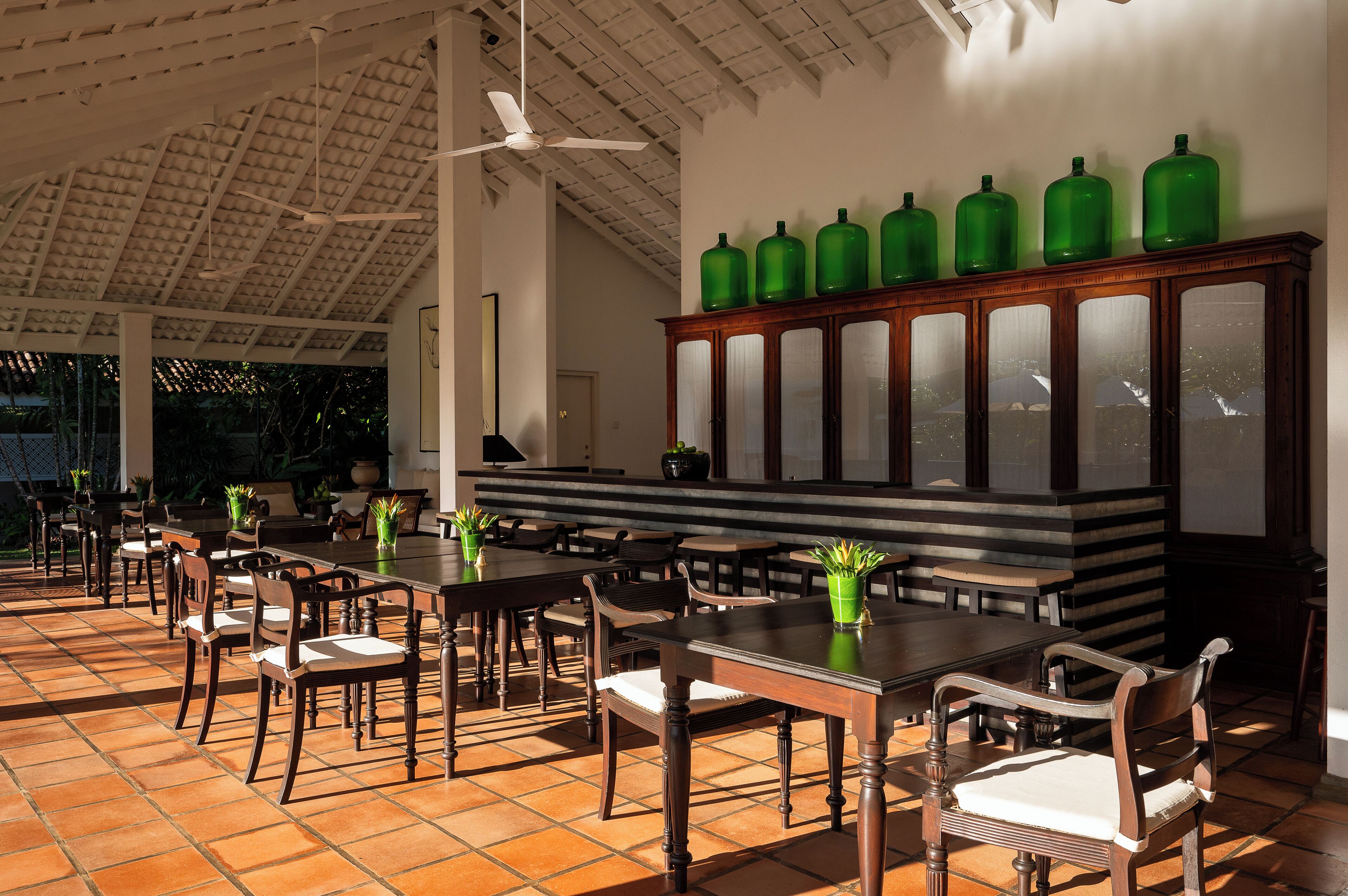 A spacious indoor dining area with wooden tables and chairs, a ceiling fan, and a cabinet with green bottles.