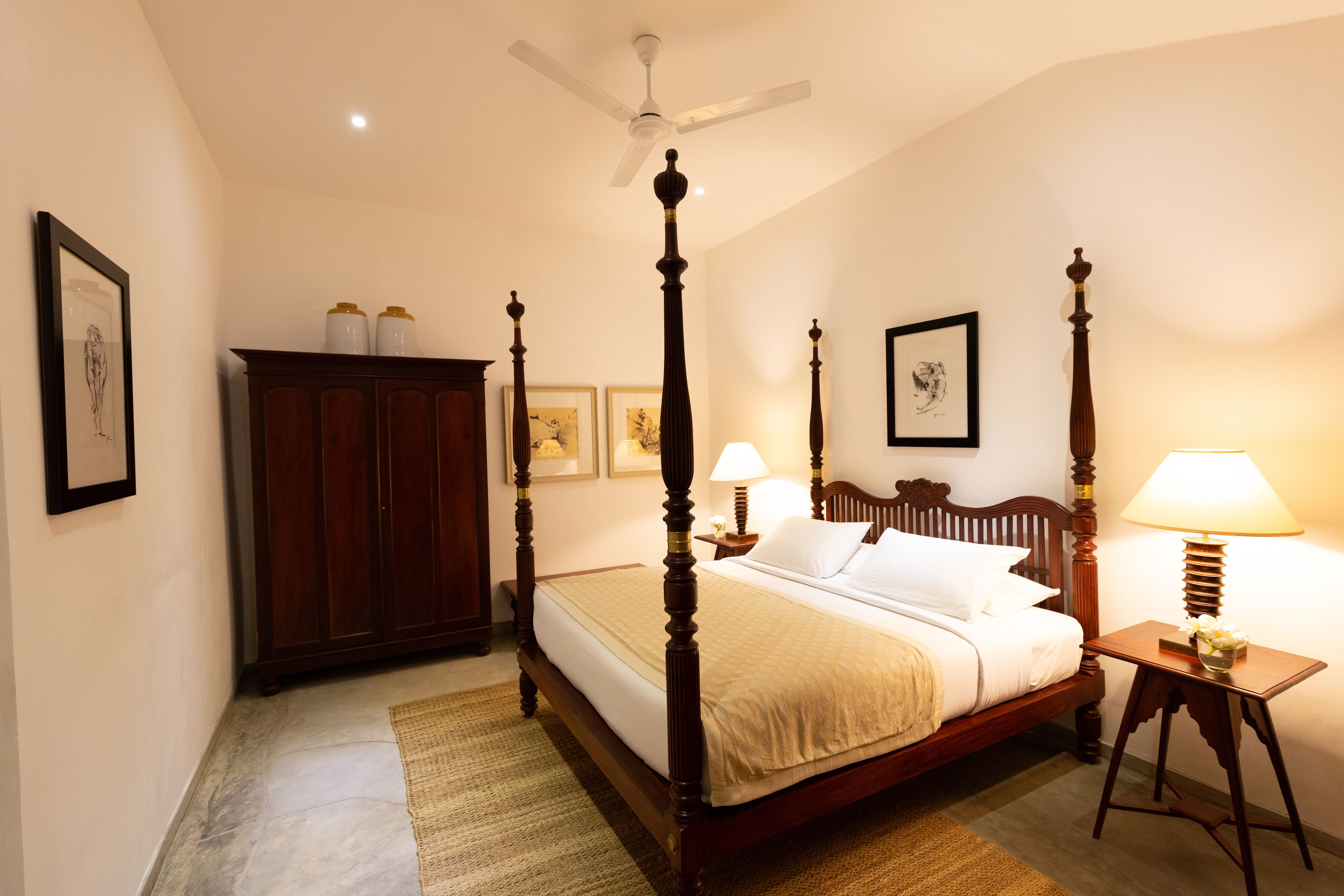 Uma cama de dossel com cabeceira de madeira, um ventilador de teto e duas luminárias de apoio.