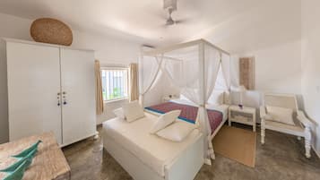 A bedroom with a four-poster bed, a white wardrobe, a bedside table with a lamp, and a chair.